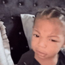 a baby is sitting on a bed with a pillow and making a funny face .