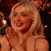 a woman is clapping her hands and smiling at the camera