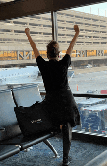 a woman with her arms in the air is looking out a window at an eagle airplane