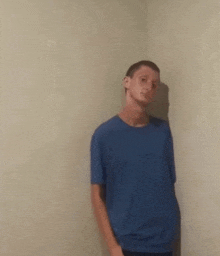 a young man in a blue shirt is standing in a corner .