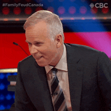 a man in a suit and tie is sitting in front of a microphone with the words family feud canada behind him