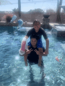 a boy in a black shirt is carrying another boy in a swimming pool