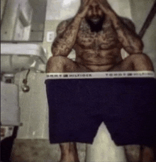 a shirtless man sits on a toilet with his tommy hilfiger underwear on