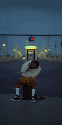 a man sits in front of a payphone that says telephone on it