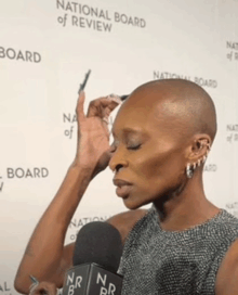 a woman holds a microphone in front of a national board of review sign