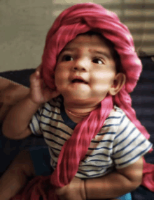 a baby wearing a striped shirt and a pink head scarf