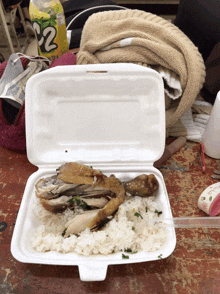 a styrofoam container filled with rice and meat next to a can of s2 extra tea