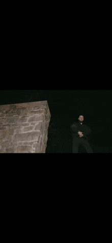 a man in a black jacket is standing on a ledge in the dark .