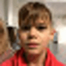 a close up of a young boy 's face wearing a red shirt .