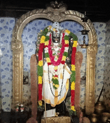 a statue of a deity in a temple with flowers around him