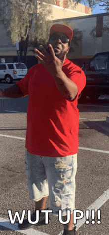 a man in a red shirt and hat is standing in a parking lot with the words wut up written below him