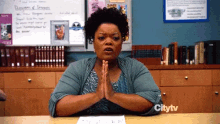 a woman sits at a desk with her hands folded in front of a sign that says citytv on it