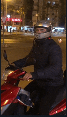 a man wearing a helmet is riding a red scooter in front of a red sign that says i merkez