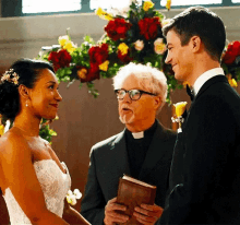 a bride and groom are holding hands during their wedding ceremony while a priest holds a bible .