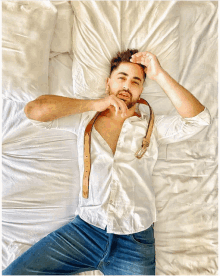 a man in a white shirt and blue jeans is laying on a white bed