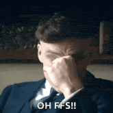a man in a suit is covering his face with his hand .