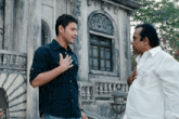 a man in a black shirt is talking to another man in a white shirt in front of a building