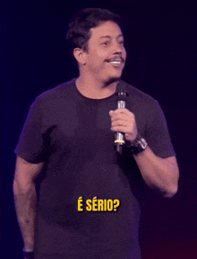 a man in a black shirt is holding a microphone and says " e serio " in yellow