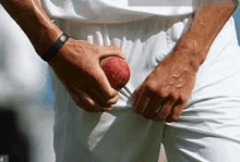 a man in white pants is holding a cricket ball in his pocket .