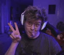 a man wearing headphones and glasses is sticking his tongue out while making a peace sign .