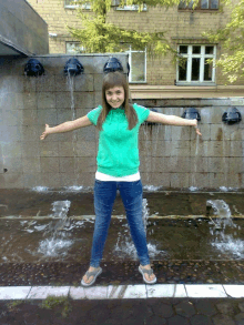 a girl in a green shirt stands in front of a waterfall