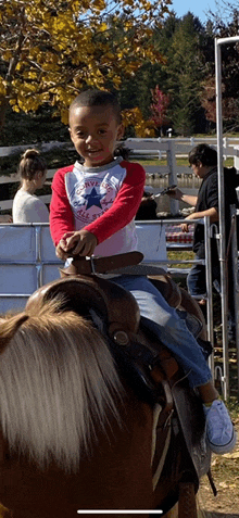 a young boy wearing a converse shirt sits on a horse