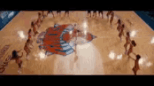 a group of women are dancing on a basketball court in front of a logo for the new york knicks .