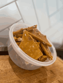 a plastic container of peanut brittle sits on a wooden table