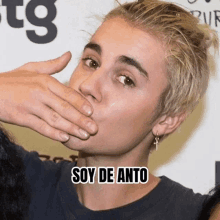 justin bieber is covering his mouth with his hand and the words soy de anto are below him