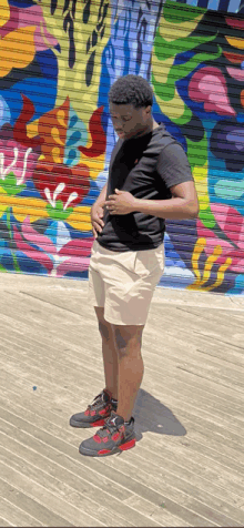 a young man is standing in front of a colorful mural on a wall .