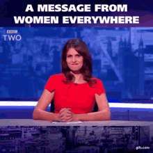 a woman in a red shirt is sitting at a desk with a message from women everywhere written above her