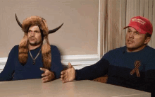 two men wearing trump hats are sitting at a desk