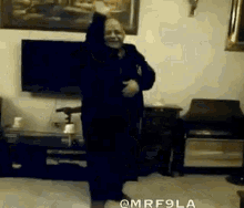 an elderly man is dancing in a living room with his arms in the air .