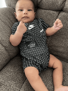 a baby wearing a black nike outfit laying on a couch