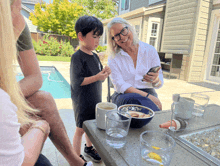 a woman sits at a table with a bowl of food and a child looking at her phone