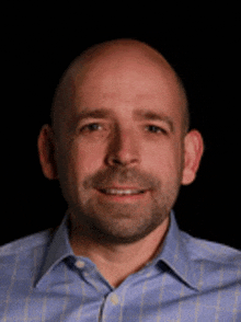 a bald man with a beard wearing a blue plaid shirt smiles for the camera .