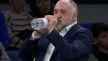 a man in a suit is drinking water from a bottle that says aquafina on it