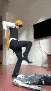 a person wearing a yellow scarf and black pants is dancing in a living room