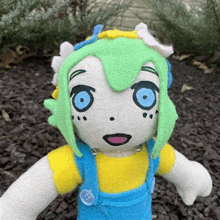 a stuffed doll with green hair and blue eyes is standing on a pile of gravel .