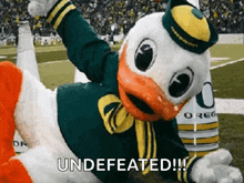 a duck mascot is laying on the ground with the words " undefeated " written below him .