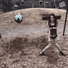 a girl in a black tank top is standing in front of a playground with a jukin video sign in the background