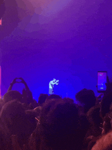 a man stands on stage in front of a crowd while a phone displays the time of the show