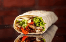 a tortilla wrap with meat lettuce and tomatoes