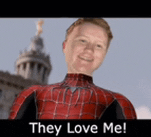 a man in a spiderman suit is standing in front of a building with the words `` they love me '' .