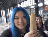a girl with blue hair is holding a sandwich in front of a 7 eleven