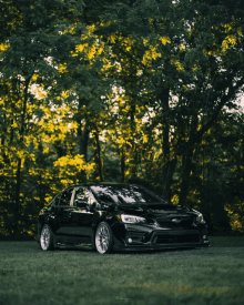 a black car is parked in a grassy area with trees behind it