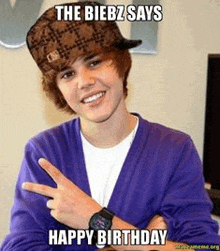 justin bieber is wearing a purple cardigan and a hat and giving a peace sign .