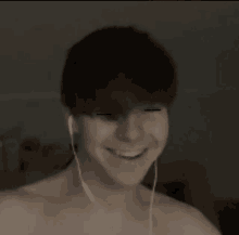 a shirtless man wearing ear buds smiles in a dark room