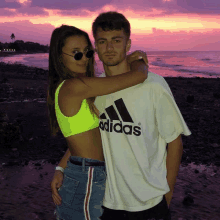 a man wearing an adidas shirt hugs a woman on the beach