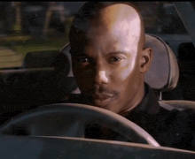 a man in a black shirt is driving a car and looking at the camera